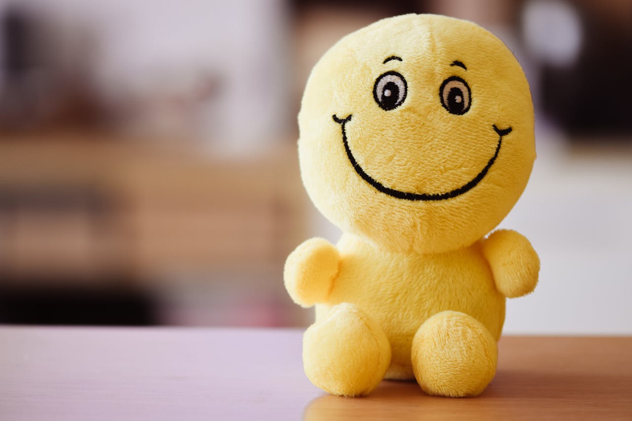 A bright yellow plush toy with a smiley face sitting on a wooden table, radiating joy.